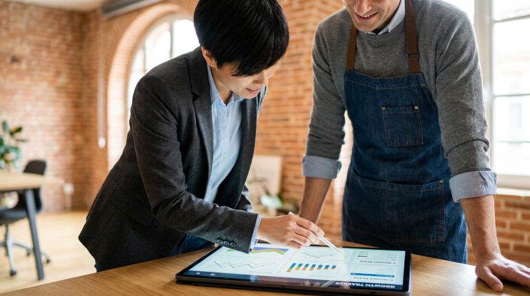 Un expert-comptable conseille un artisan sur des graphiques de croissance affichés sur une tablette.
